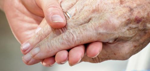 Nahaufnahme zweier Hände, eine ältere und eine jüngere, die sich liebevoll halten.